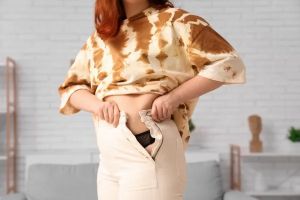 Image of woman trying to do her trousers up after pregnancy weight gain Burton upon Trent