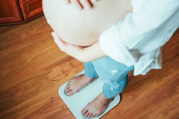 Image of woman weighing herself and experiencing weight gain through pregnancy Burton upon Trent
